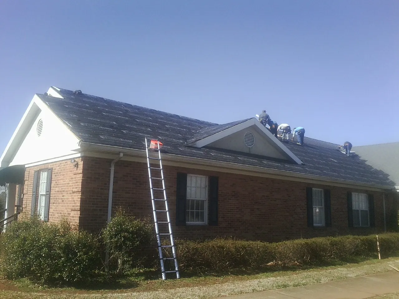 Crew tearing shingles off a brick ranch roof with a ladder set — Metal Roof Repair work by our crew in Clarkton
