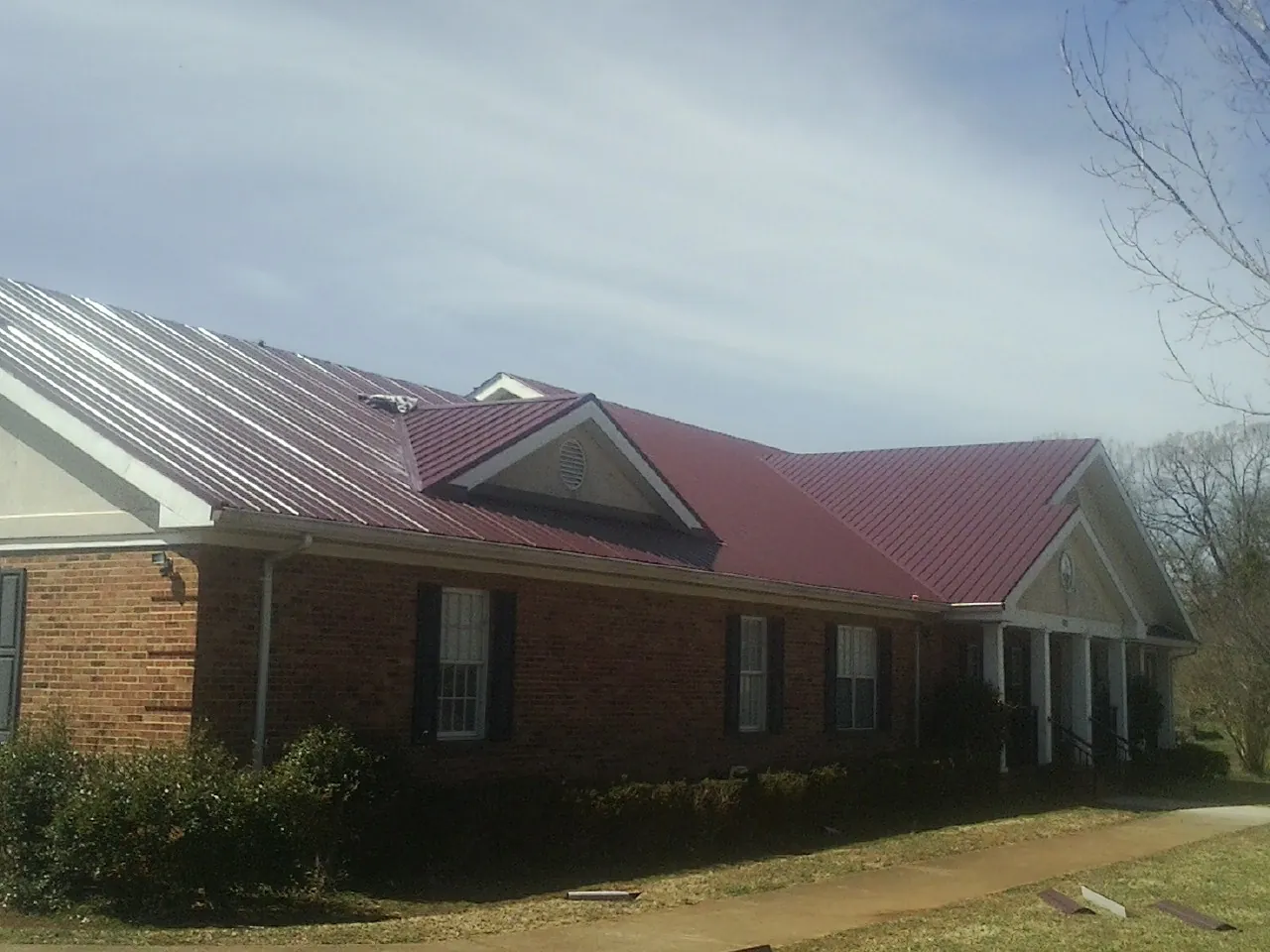 Red metal roof with gabled entries on a long brick building, from a Hail Damage Roof Repair job in Clarkton