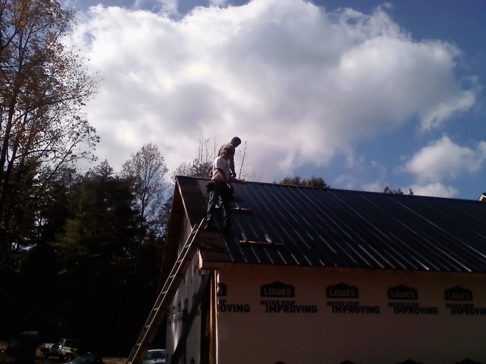 Roofer fastening dark metal panels high against a cloudy sky, from a Roof Inspection job in Clarkton