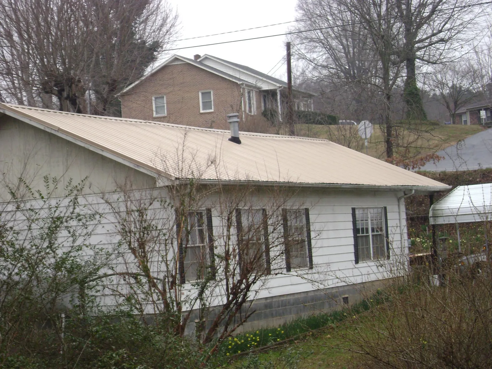 Tan metal roof on a white sided house set into a hillside — Commercial Roofing by Roofing Brothers in Clarkton
